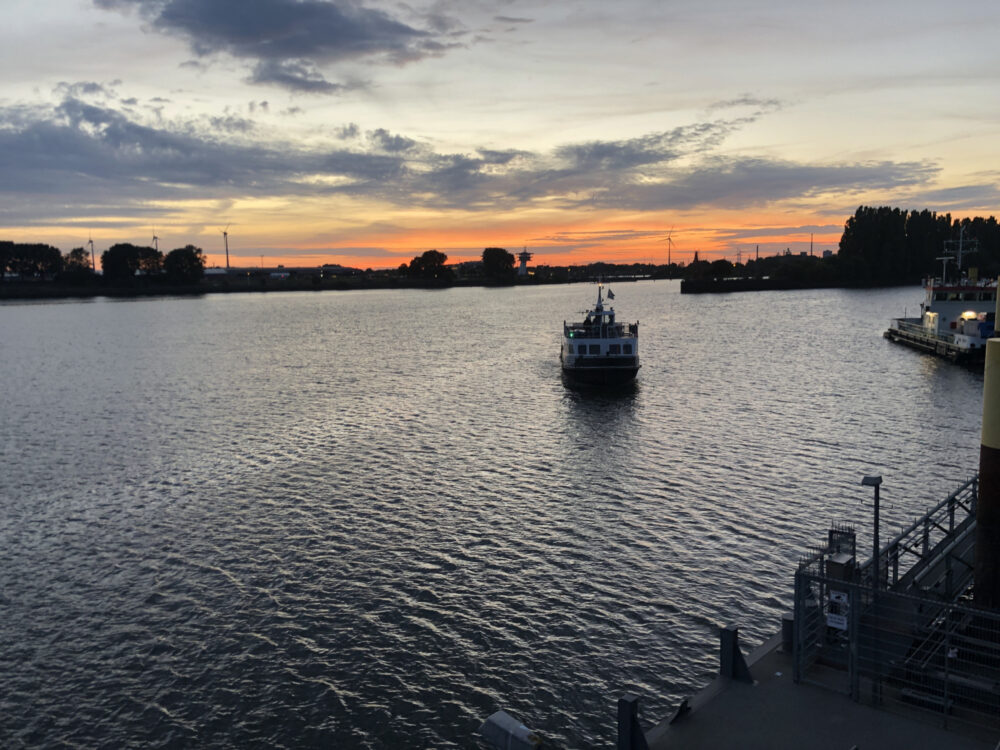 Ein Fahrgastschiff nähert sich auf dem Fluss einem Anleger bei Sonnenuntergang.