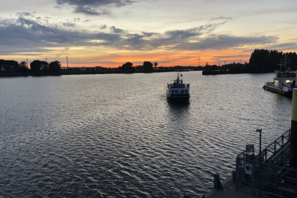 Ein Fahrgastschiff nähert sich auf dem Fluss einem Anleger bei Sonnenuntergang.