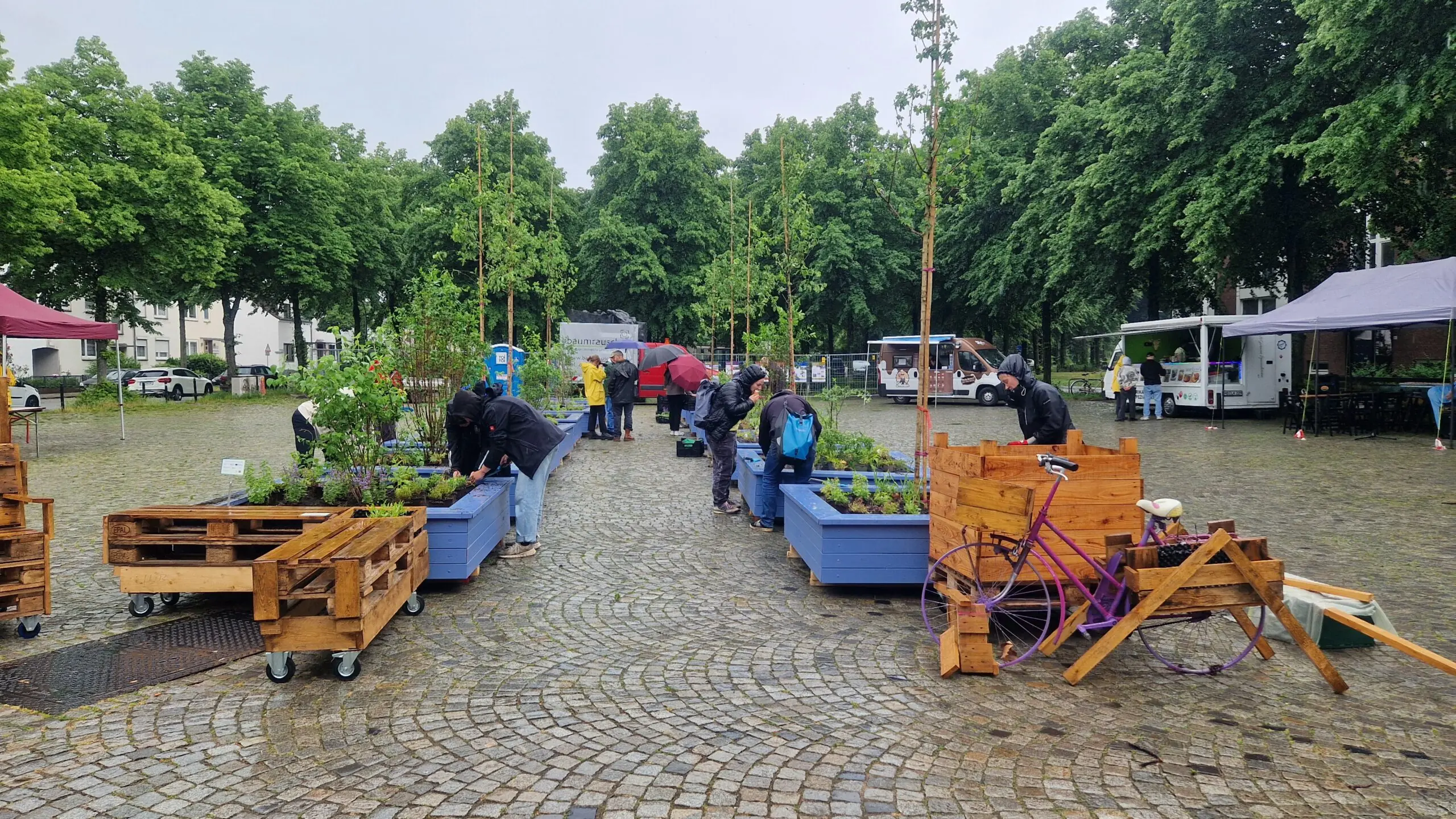 Der gepflasterte Bürgermeister-Ehlers-Platz in Gröpelingen mit neuen mobilen Hochbeeten. Einige Menschen sind dabei, die Beete zu bepflanzen.