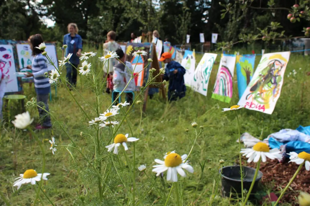 Zu sehen ist die Blumenwiese hinter dem Gröpelinger Strassenbahndepot. Kinder hängen ihre Bilder auf einer Wäscheleine zum Trocknen auf.