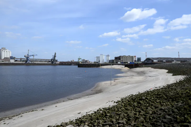 Ein Hafenbecken mit einem Sandstrand ist zu sehen.