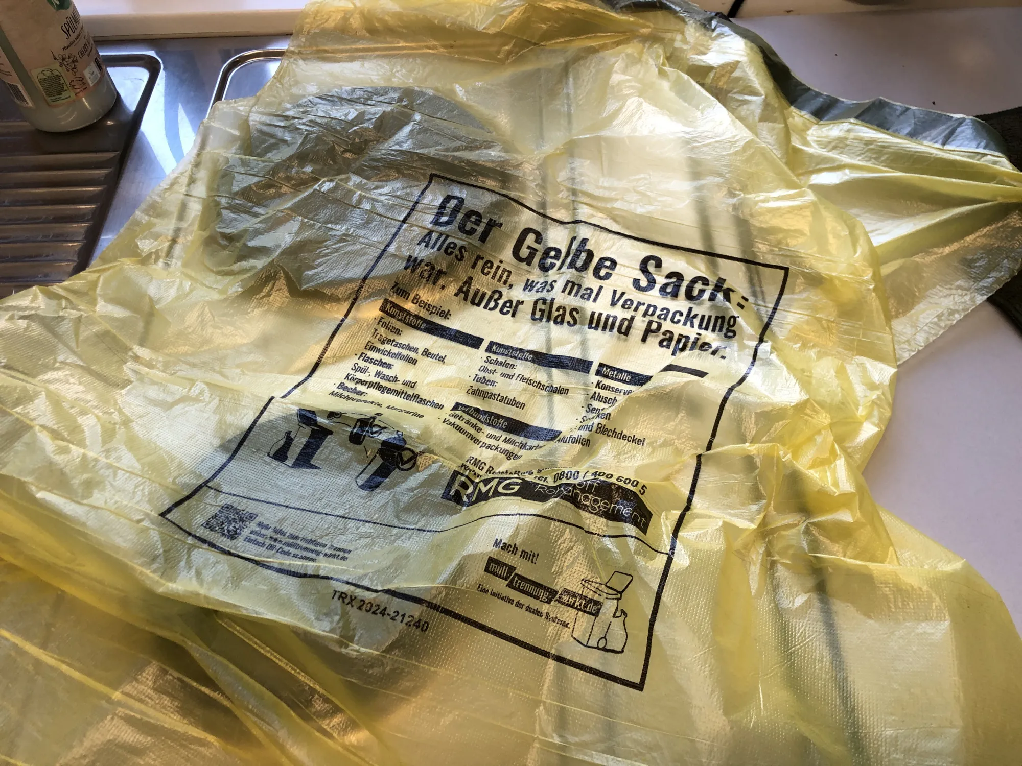 Auf einer Kochniesche liegt ein leerer Gelber Sack. Die Beschriftung was rein soll und was nicht ist gut zu lesen.
